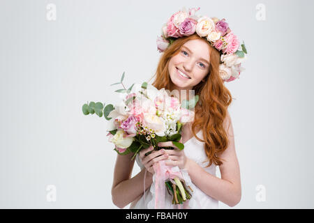 Lächelnd attraktive junge Frau mit langen roten Haaren in Kranz mit Blumenstrauß auf weißem Hintergrund Stockfoto