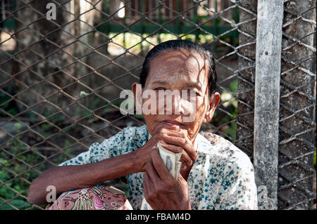 Eine alte burmesische Dame sitzt auf dem Bürgersteig vor einem Drahtzaun auf eine Straße von Rangun Myanmar Burma betteln Stockfoto