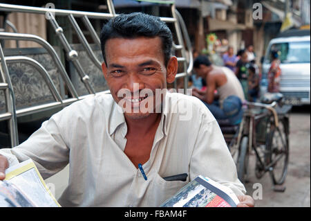 Happy burmesischen Rikscha Fahrer sieht von seiner Zeitung auf seinem rikscha taxi Yangon Myanmar sitzen Stockfoto