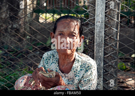 Eine alte burmesische Dame sitzt auf dem Bürgersteig vor einem Drahtzaun auf eine Straße von Rangun Myanmar Burma betteln Stockfoto