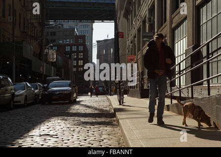 Mann zu Fuß einen Hund auf einer Kopfsteinpflaster bedeckt Water Street in Brooklyn Bridge, DUMBO Nachbarschaft. Stockfoto