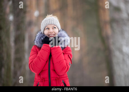 Lächelndes schöne Mädchen Strickmütze und roten Wintermantel sich einwickeln in Pelzkragen, im freien Stockfoto