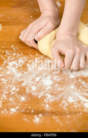 Schließen Sie Hausmannskost, weibliche Hände kneten Paste auf Holztisch mit Mehl bedeckt Stockfoto