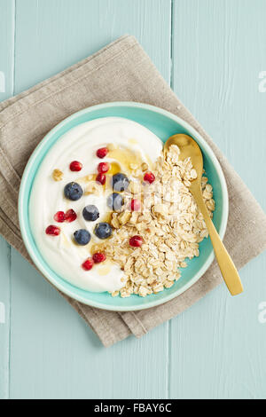 Frühstück-Hafer-Müsli mit Heidelbeeren, Granatapfel-Samen, Nüssen, Honig und Joghurt mit einem goldenen Löffel in eine Schüssel geben Stockfoto