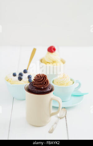 Vanille und Schokolade Becher Kuchen mit Heidelbeeren und Himbeeren mit Löffeln auf einem Tisch Stockfoto