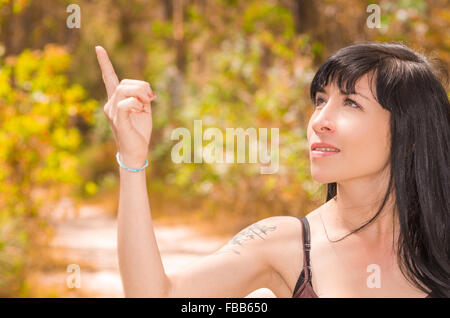 Hübsche Brünette im Wald Umwelt Closeup hochhalten Punkt Finger und lächelnd Stockfoto