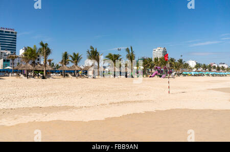 Palmen Sie am Strand von Da Nang, Vietnam. Eine rote Fahne fliegt. Hotels und ein Kinderspielplatz im Hintergrund. Stockfoto