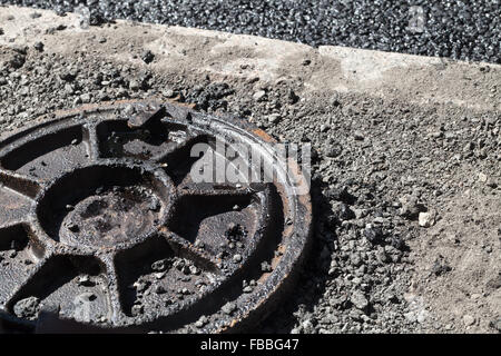 Städtische Straße im Bau, Asphaltierung im Gange. Schmutzige verrosteten Kanalisation Kanaldeckel legt auf einem Straßenrand Stockfoto