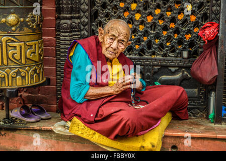 Sehr alte tibetische buddhistische Nonne sitzt und bittet vor einem Heiligtum in Kathmandu Stockfoto