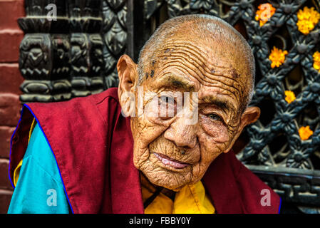 Sehr alte tibetische buddhistische Nonne sitzt vor einem Heiligtum in Kathmandu Stockfoto