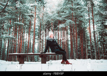 Schlankes Mädchen sitzt auf einer Bank im Winter. Stockfoto