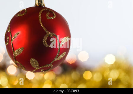 Rote Christbaumkugel mit gold Lametta und Lichterketten hinter. Stockfoto