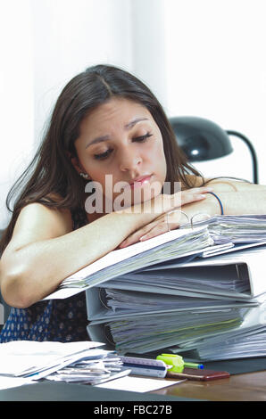 Hispanische Brünette Büroangestellten durch Schreibtisch sitzen und liegen über Haufen von Archivdateien suchen müde Stockfoto
