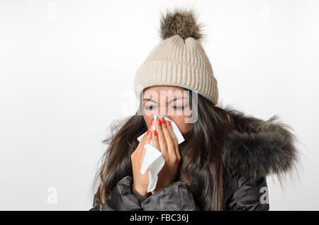 Junge Frau mit einem saisonalen Winterkälte und Grippe gekleidet in warme trendige Kleidung, die ihre Nase auf ein weißes Taschentuch Stockfoto