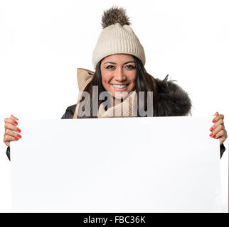 Attraktive Frau im Winter Fashion holding ein leeres weißes Schild mit textfreiraum an ihre Brust als sie schaut die Kamera mit einem lov Stockfoto