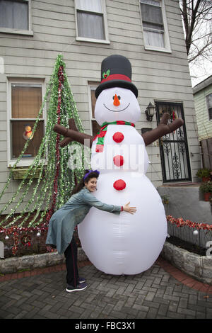 Frau umarmt aufblasbare Schneemann Weihnachtsdekoration vor einem Haus in Brooklyn, New York. Stockfoto