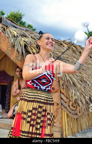 Maori-Frau und Maori-Mann in Te Puia Maori Village Rotorua. Frau tanzt mit POI(s), während der Mann in der Hütte dahinter ist. Nordinsel, Neuseeland Stockfoto