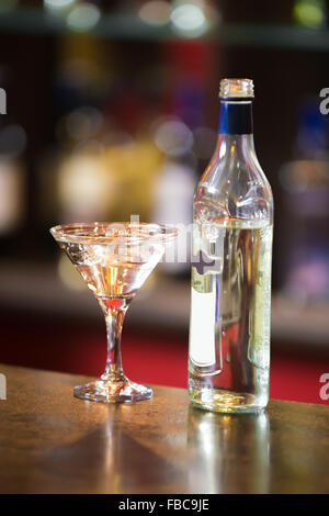 Flasche und Alkoholiker trinken mit Eiswürfeln und Olive im Martini-Glas auf Bartheke Stockfoto