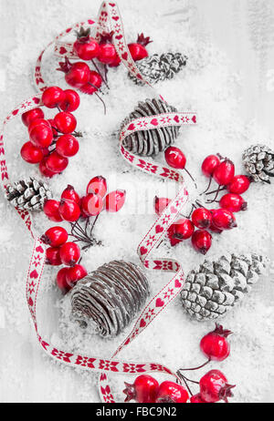 Weihnachts-Dekoration Band mit roten Beeren und Zapfen im Schnee auf lackiertem Holz Stockfoto