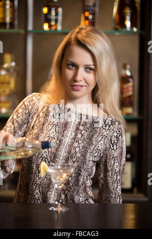 Arbeiten blonden weiblichen Barkeeper, cocktail am Tresen zu machen, halten Sie die Flasche in der hand, Gießen Getränk in Martini-Glas Stockfoto