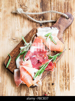 Serrano Schinken mit Rosmarin und Pfeffer Gewürz auf einem Holzbrett Stockfoto