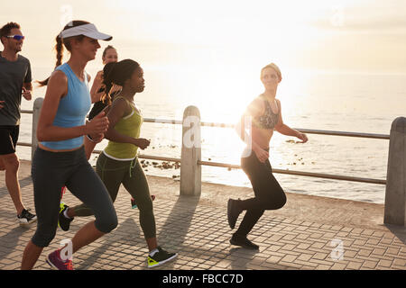 Junge Menschen, die entlang am Meer bei Sonnenuntergang. Nahaufnahme Bild der Gruppe von Läufern, die Arbeiten auf einer Straße am Meer. Stockfoto