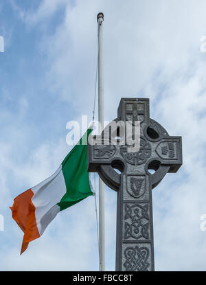 Eine irische Trikolore fliegt auf einem Mast hinter eine traditionelle irische keltische Kreuz auf Halbmast. Stockfoto
