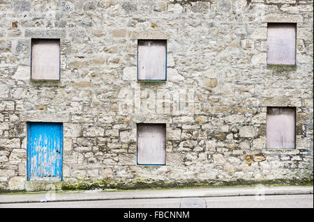 Teil der Fassade ein altes Steinhaus in Schottland mit Brettern vernagelt Windows eine blaue Holztür Stockfoto