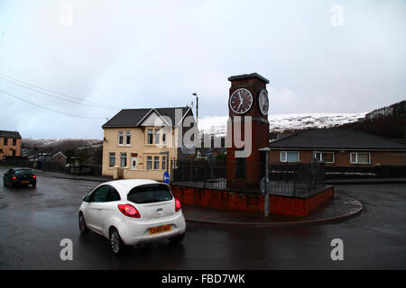 Nant y Moel, Mid Glamorgan, Südwales. 15th. Januar 2016: In einem Kreisverkehr auf der Straße A4061 im Dorf Nant y Moel im oberen Ogmore Valley in Südwales fährt ein Auto am Uhrenturm vorbei, mit frischem Schneefall auf den Mynydd Llangeinwyr Hügeln dahinter. Mehrere Zentimeter Schnee fielen über Nacht auf die Hügel, was das Met Office dazu veranlasste, eine Unwetterwarnung über Schnee und Eis für die Region mit gelbem Niveau auszustellen. Quelle: James Brunker/Alamy Live News Stockfoto