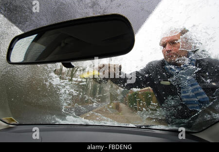 Ein Mann ist das Eis von der Windschutzscheibe seines Autos kratzen. Stockfoto