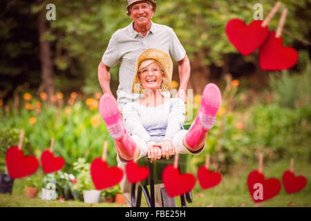 Zusammengesetztes Bild von glücklichen senior paar spielen mit einer Schubkarre Stockfoto