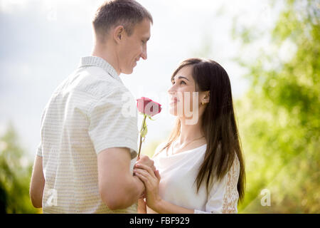 Liebespaar treffen auf ein Datum, jungen Mann eine rote Rose, seine schöne brunet Freundin mit langen Haaren Stockfoto