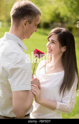 Liebespaar treffen auf ein Datum, auf der Suche in einander in die Augen, junger Mann, seine schönen glücklich lächelnde Brunet rote rose verleihen Stockfoto