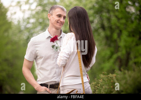 Liebespaar im Park, an einem Tag treffen suchen einander in die Augen, lächelnd jungen Mann seine brunet Girlfrie rote rose verleihen Stockfoto