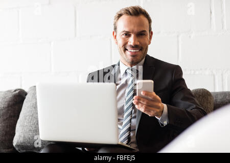 Lächelnde Geschäftsmann mit Laptop und smartphone Stockfoto