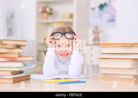 Kleine positive Mädchen ist an der Rezeption mit vielen Büchern. Stockfoto