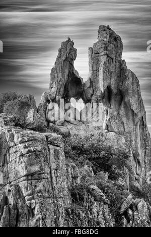 B&W Bild der herzförmige Loch in den Felsen an den Calanches de Piana an der West Küste von Korsika mit blauem Himmel hinter Stockfoto