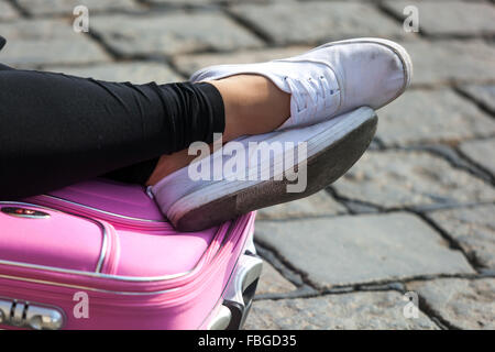 Ruhende Mädchen Beine in Turnschuhen auf einem rosa Koffer Stockfoto