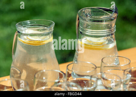 Die zwei Karafes mit frischem Wasser mit Zitronengeschmack und Gläser auf einem Tisch im Garten