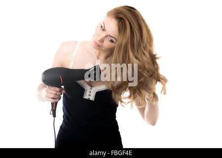 Portrait von junge wunderschöne, blonde Kaukasische Frau mit schwarzen Fön trocknen ihre schönen langen Haare mit glücklichen Lächeln, Studio Stockfoto