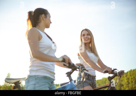 Zwei glückliche Lächeln schöne Mädchen im Teenageralter in Jeans Shorts auf Fahrrädern gegen blauen Himmel auf sonnigen Sommertag mit guter tim Stockfoto