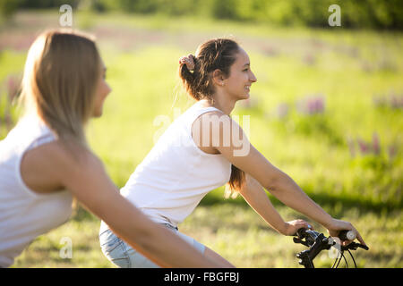Zwei süße junge glücklich lächelnd schöne Freundinnen tragen lässige weiße Unterhemden zu genießen, Radfahren im Park an sonnigen Sommertag, foc Stockfoto