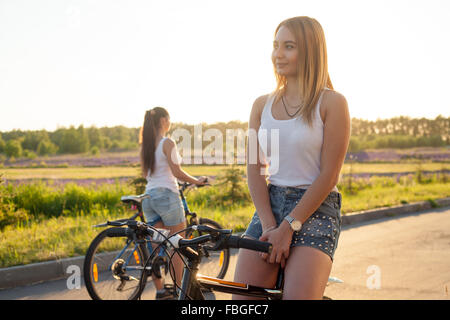 Schöne blonde junge Frau sitzt auf Sportmotorrad tragen legere Kleidung auf der Straße an hellen, sonnigen Sommertag, auf der Suche nach somewhe Stockfoto