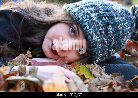 Schöne Teenager-Mädchen liegend auf einem Bett aus bunten Blättern im Herbst direkt an Kamera Stockfoto