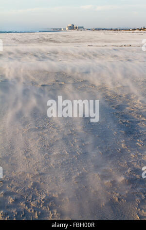 Starker Wind bläst Sand über den Strand mit Koeberg Atomkraftwerk im Hintergrund. Stockfoto