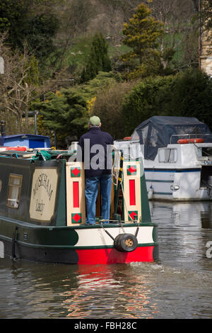 Mann an der Deichsel, steuert die traditionellen Narrowboat entlang Leeds Liverpool Canal Vergangenheit modernen Cruiser in der Nähe - Bingley, West Yorkshire, England, GB, UK. Stockfoto