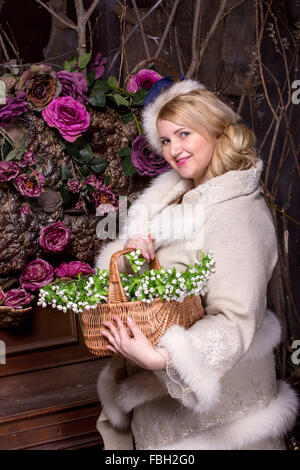 Ziemlich, Plus Size Frau mit Korb mit Frühlingsblumen im Mantel mit Fell Trimmen auf dunkle Blume Hintergrund Stockfoto