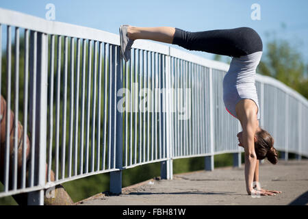 Yoga in der Stadt: schöne sportliche junge Frau, die Arbeiten auf der alten Brücke, stützte sich auf Geländer in Variation der Adho Mukha Vrks Stockfoto