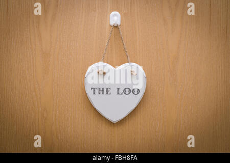 Weiße Zeichen für die Toilette, WC hängend an einem weißen Haken auf eine Holztür in Herzform Stockfoto
