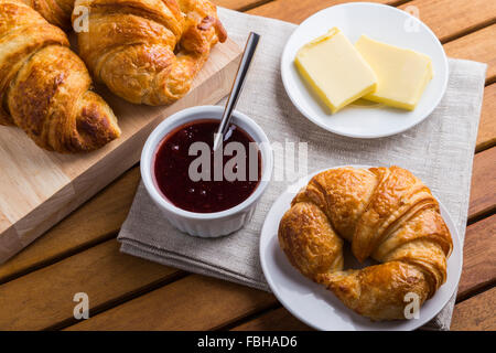 Croissants, Marmelade und Butter auf hölzernen Tisch Stockfoto